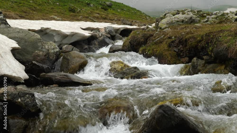 A clear stream runs over stone boulders in the mountains. Water runs in rapids along the stone bed. Wildlife. Behind in the background of the mountain in the fog. Background video A clear stream runs over stone boulders in the mountains. Water runs in rapids along the stone bed. Wildlife. Behind in the background of the mountain in the fog. Background video