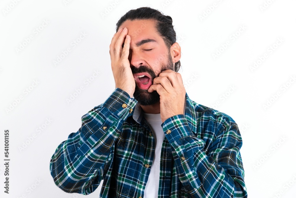 Young gloomy young bearded hispanic man wearing plaid shirt over white background, hiding face with hands pouting and crying, standing upset and depressed complaining about job problem. Young gloomy young bearded hispanic man wearing plaid shirt over white background, hiding face with hands pouting and crying, standing upset and depressed complaining about job problem.