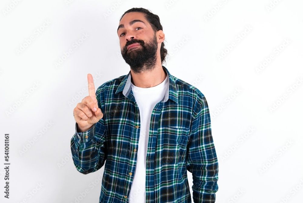No sign gesture. Closeup portrait unhappy young bearded hispanic man wearing plaid shirt over white background raising fore finger up saying no. Negative emotions facial expressions, feelings. No sign gesture. Closeup portrait unhappy young bearded hispanic man wearing plaid shirt over white background raising fore finger up saying no. Negative emotions facial expressions, feelings.
