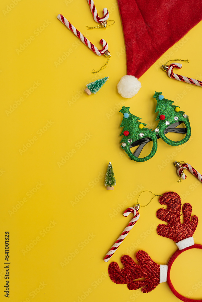 Funny New Year, Christmas accessories for winter holidays party celebration on yellow background. Christmas eyeglasses, candy canes, deer horns, Santa hat, toy trees