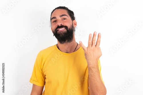 young bearded hispanic man wearing yellow T-shirt over white background smiling and looking friendly, showing number four or fourth with hand forward, counting down