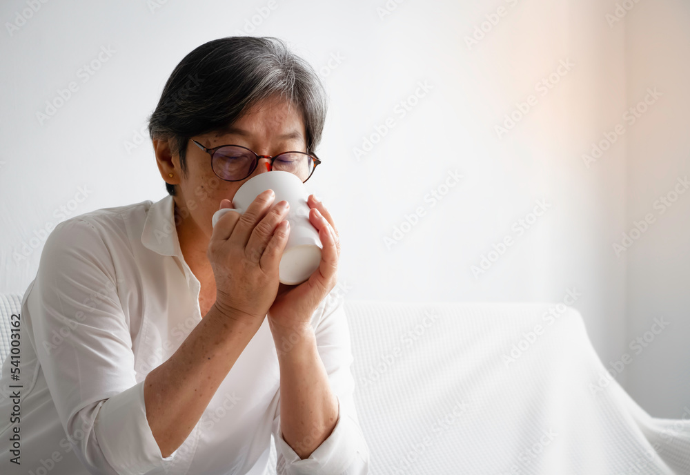 Old smart lady with gray hair wearing glasses,hold ceramic cup in hands and drink Old smart lady with gray hair wearing glasses,hold ceramic cup in hands and drink