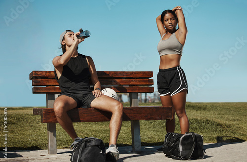 Man, woman and fitness break for stretching, drinking water or muscle recovery after training, exercise and workout. Soccer players, sports friends or football players in warmup in nature garden park photo