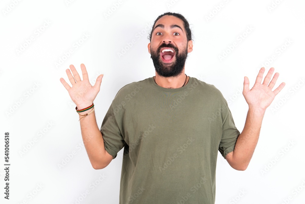 Optimistic young bearded hispanic man wearing green T-shirt over white background raises palms from joy, happy to receive awesome present from someone, shouts loudly, Excited model screaming. Optimistic young bearded hispanic man wearing green T-shirt over white background raises palms from joy, happy to receive awesome present from someone, shouts loudly, Excited model screaming.