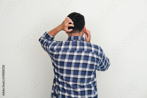 Back view of adult man scratching his head while answering a phone call photo