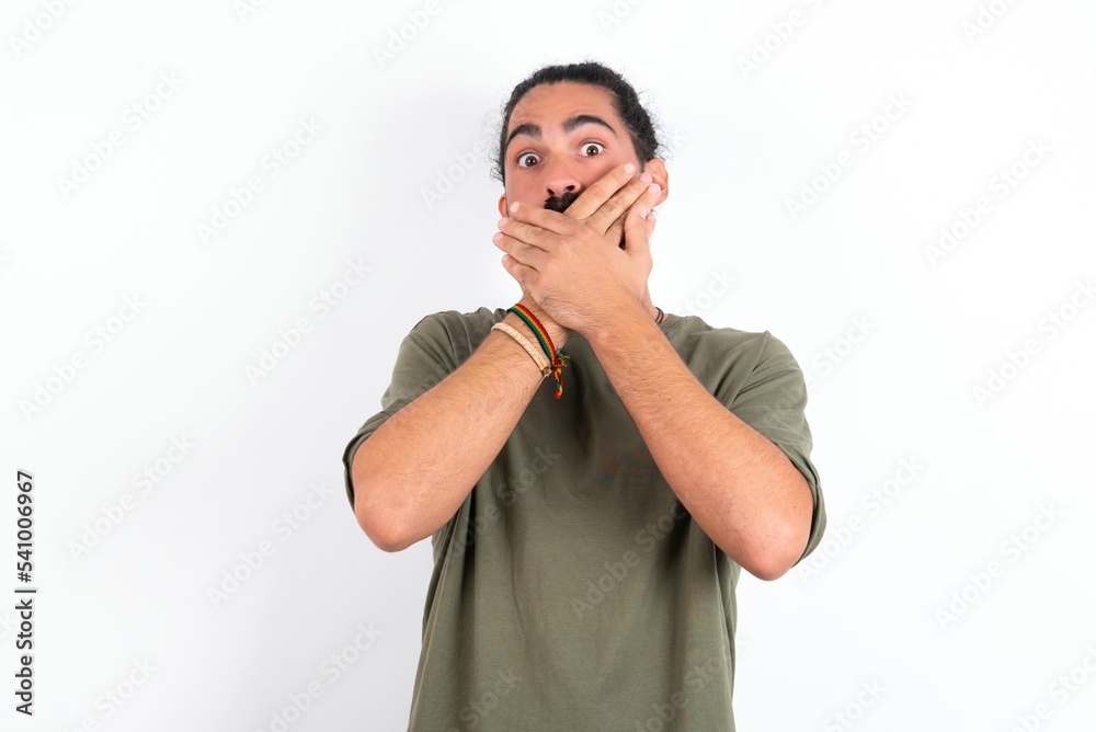 young bearded hispanic man wearing green T-shirt over white background shocked covering mouth with hands for mistake. Secret concept. young bearded hispanic man wearing green T-shirt over white background shocked covering mouth with hands for mistake. Secret concept.