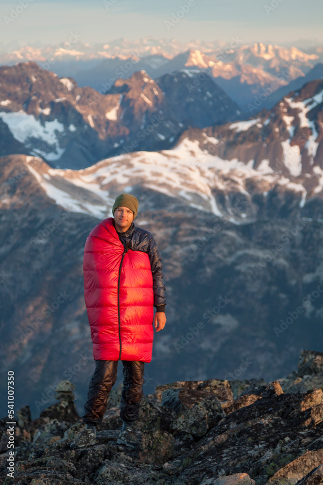 Portrait Of A Male Climber Wearing A Sleeping Bag To Stay Warm On The Summit Of A Joffre Peak Portrait Of A Male Climber Wearing A Sleeping Bag To Stay Warm On The Summit Of A Joffre Peak