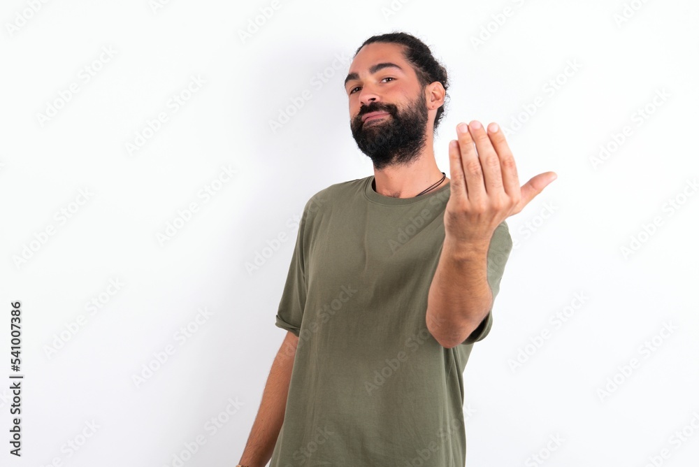 Naklejka premium young bearded hispanic man wearing green T-shirt over white background inviting to come with hand. Happy that you came