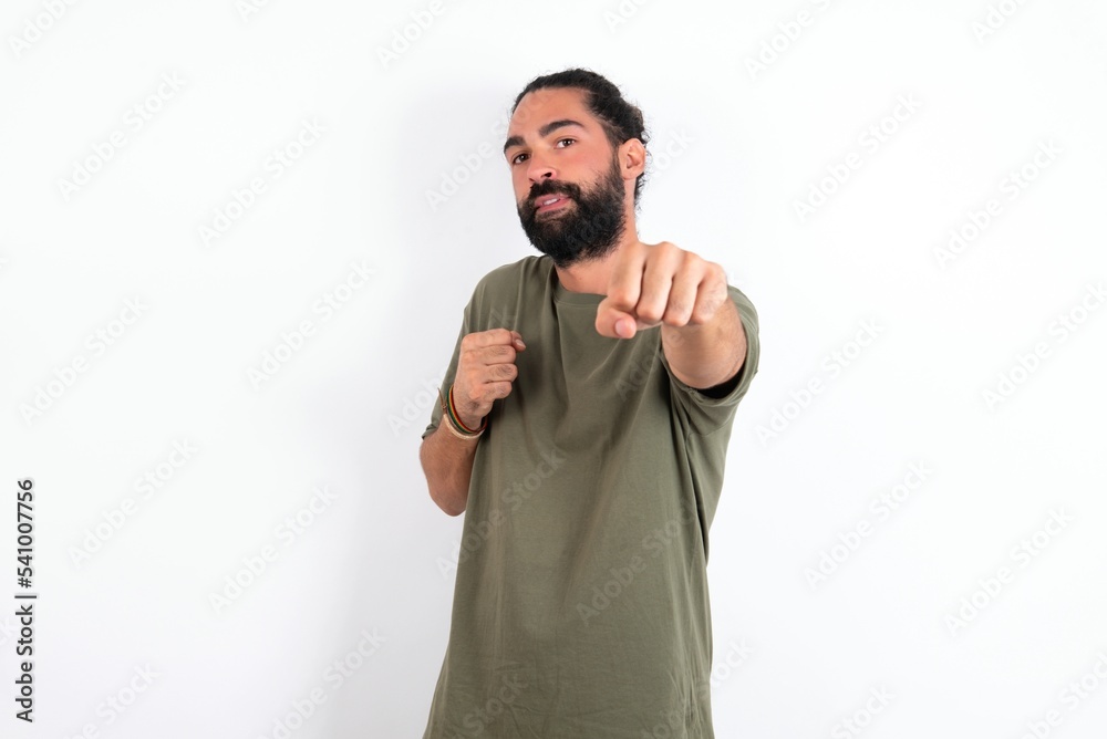 young bearded hispanic man wearing green T-shirt over white background Punching fist to fight, aggressive and angry attack, threat and violence