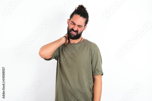 young bearded hispanic man wearing green t-shirt over white background Suffering of neck ache injury, touching neck with hand, muscular pain © Jihan