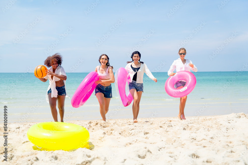 Group of teenage girls hold multicolor swim ring and ball walk back from the sea to beach with blue clear sky as background and they look happy to enjoy during holiday together. Group of teenage girls hold multicolor swim ring and ball walk back from the sea to beach with blue clear sky as background and they look happy to enjoy during holiday together.