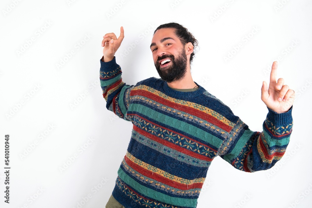 Naklejka premium Photo of upbeat Caucasian man with beard wearing sweater over white background has fun and dances carefree wear being in perfect mood makes movements. Spends free time on disco party