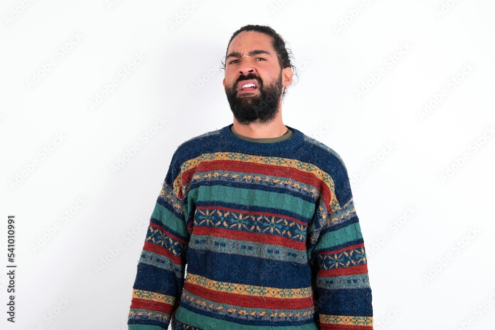 Portrait of dissatisfied Caucasian man with beard wearing sweater over white background smirks face, purses lips and looks with annoyance at camera, discontent hearing something unpleasant Portrait of dissatisfied Caucasian man with beard wearing sweater over white background smirks face, purses lips and looks with annoyance at camera, discontent hearing something unpleasant