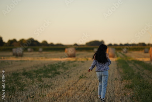 A woman in simple rural clothes and with long black disheveled hair walks through a slanted field from behind view, walking through the field alone, rural boring life © Оксана Олейник