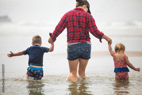 rear view of mother helping kids wade through water at the beach. photo