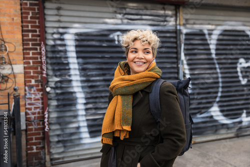 Smiling woman wearing scarf looking away while standing against closed shutter in city