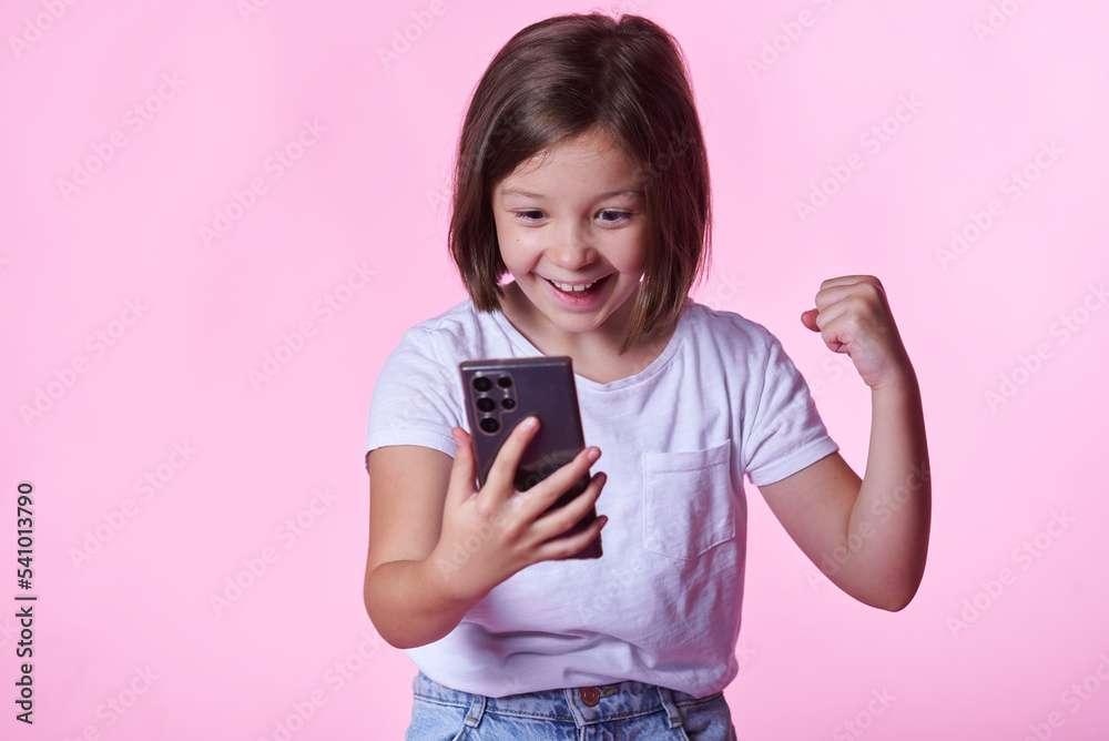 Excited little girl getting great, winning news over her phone; pink studio background Excited little girl getting great, winning news over her phone; pink studio background