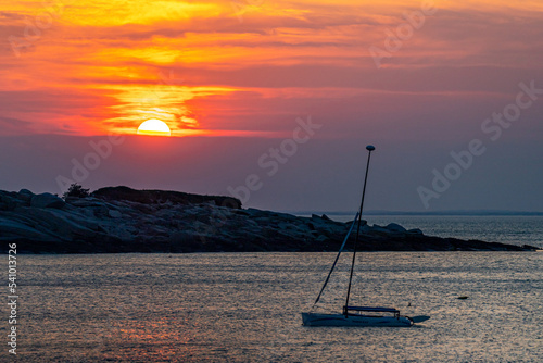 Isolated sailboat as the sun sets beyond clouds in the distance. photo