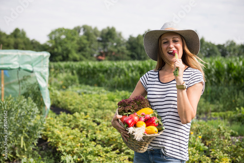 Mid adult woman eating radish and carrying vegetable basket in community garden, Bavaria, Germany photo