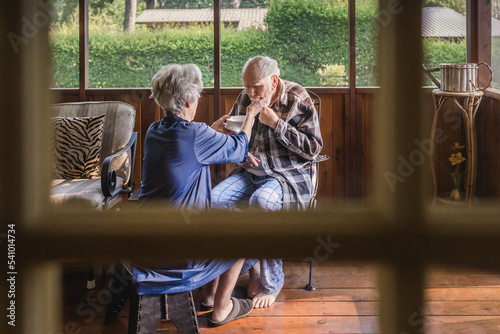 Female caretaker feeds feeble elderly man on screened porch