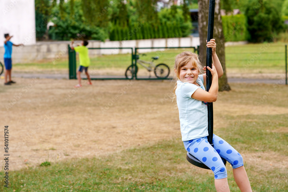 Obraz premium Happy kid girl rids on zip line swing outdoor game play equipment on playground. Child having fun outdoors. Preschool child swinging on summer day. Activity with children.
