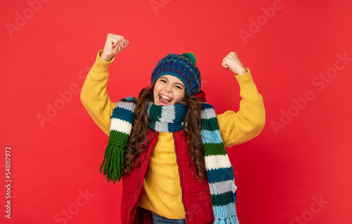 successful child in knitted winter hat and scarf on red background, success