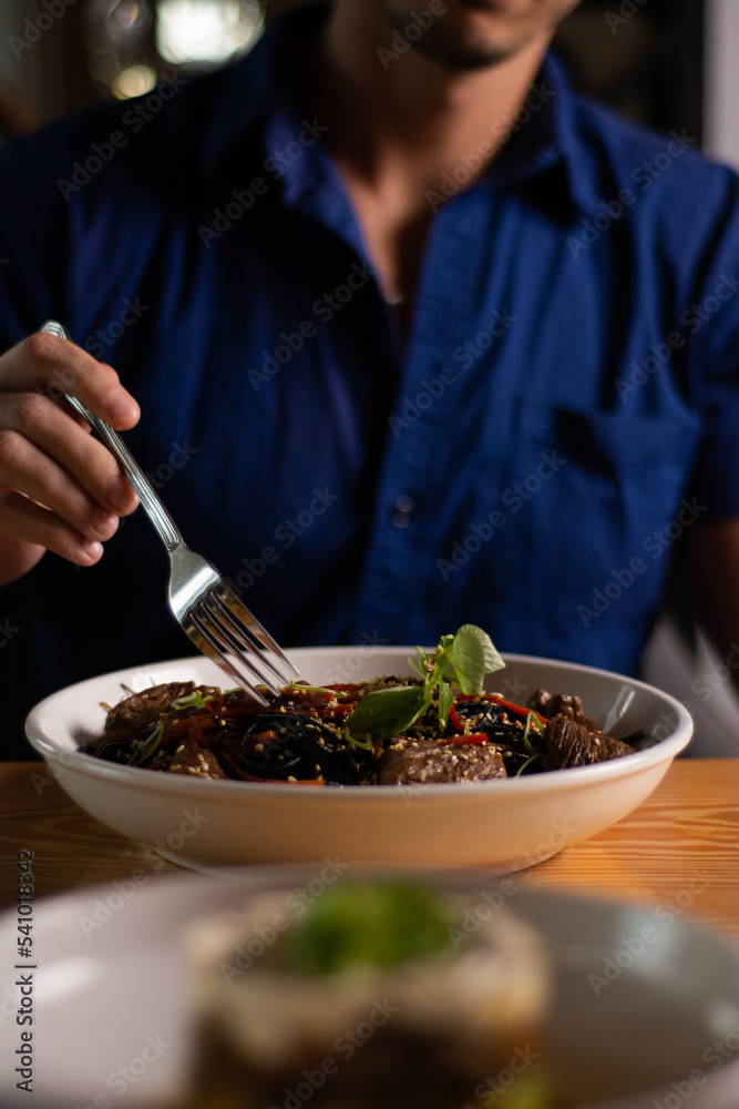 Black paste. Noodles made with squid ink. Pasta with seafood. Man in blue shirt eating
Black paste. Noodles made with squid ink. Pasta with seafood. Man in blue shirt eating