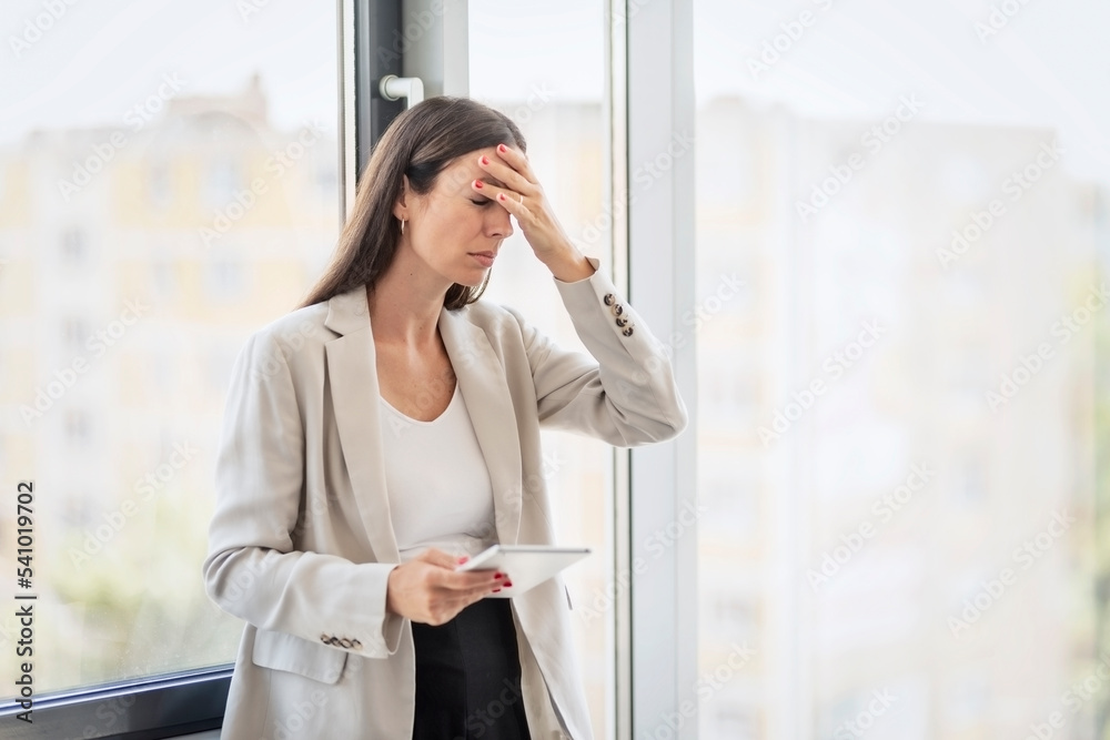Stressed businesswoman rubbing her head while standing at the office Stressed businesswoman rubbing her head while standing at the office
