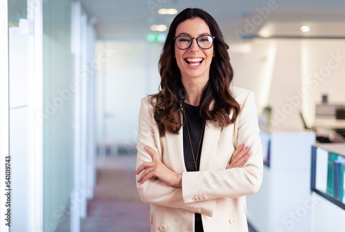 Happy businesswoman wearing glasses and blazer while standing at the office