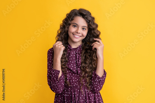 happy child with long brunette frizz hair on yellow background photo