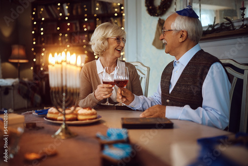 Happy senior couple toasting with wine while celebrating Hanukkah at home.