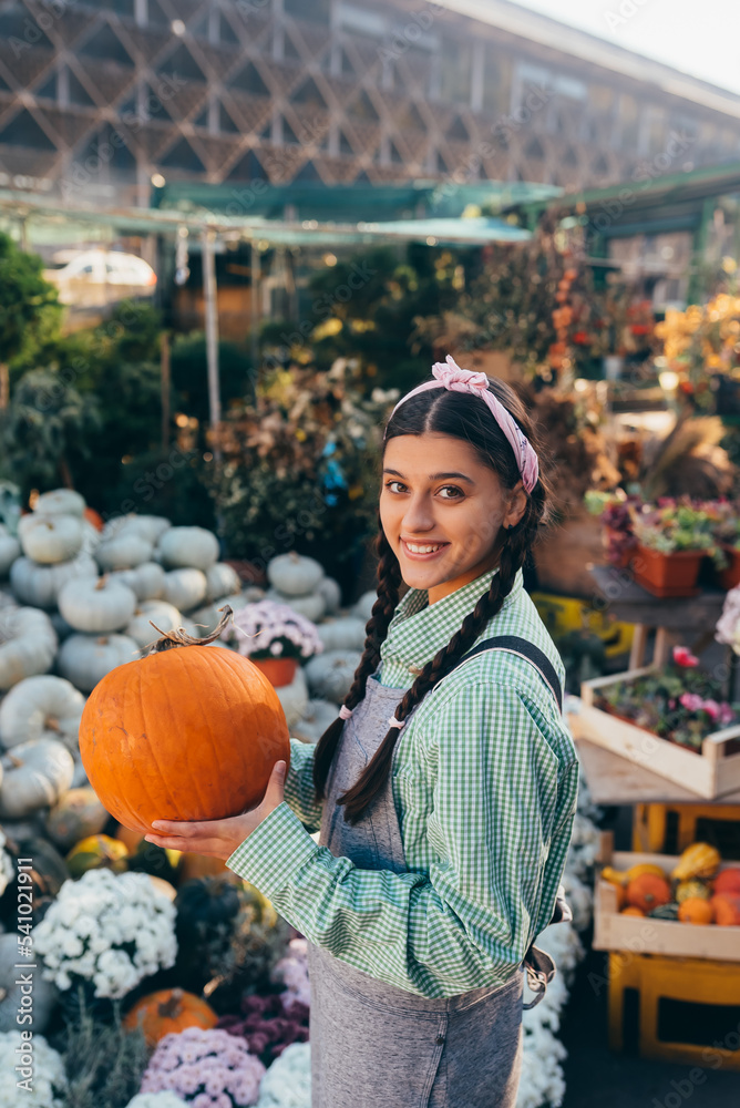 Fototapeta premium Happy farmer woman in a denim jumpsuit holds ripe pumpkin