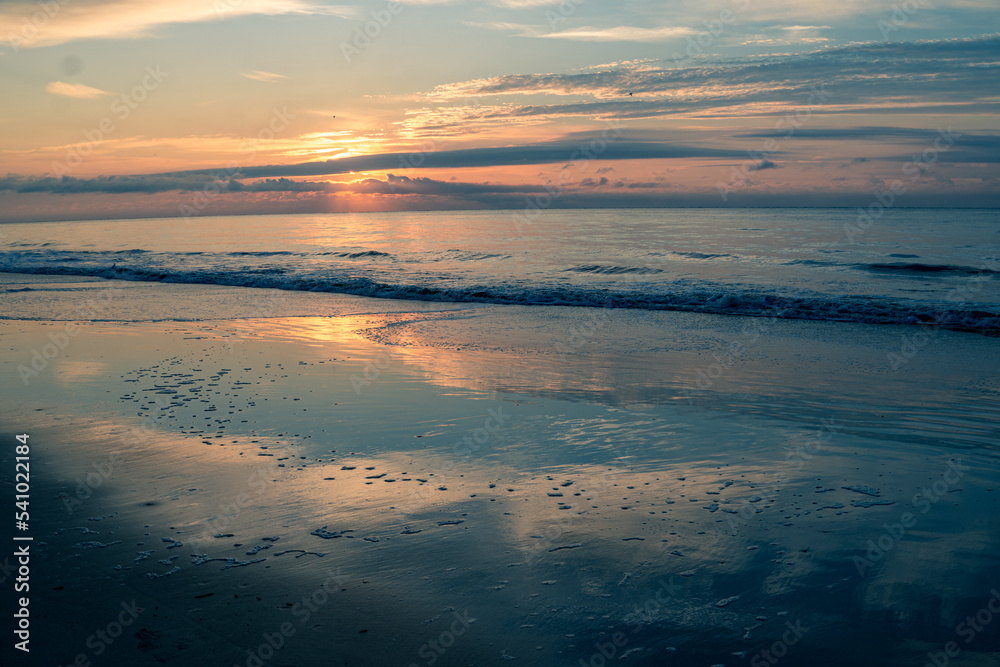 Sunrise on the beach with the sky reflecting on the wet sand
