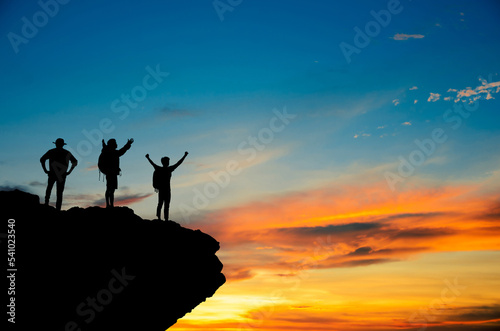 A silhouette of a small group of highly confident tourists standing with their arms raised under the sunrise on the top of the mountain. They were extremely happy and they showed victory.