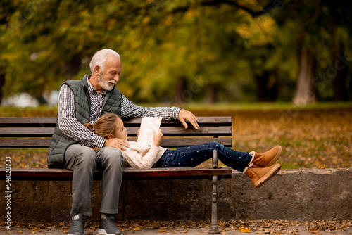 Print op canvas Grandfather spending time with his granddaughter on bench in park on autumn day