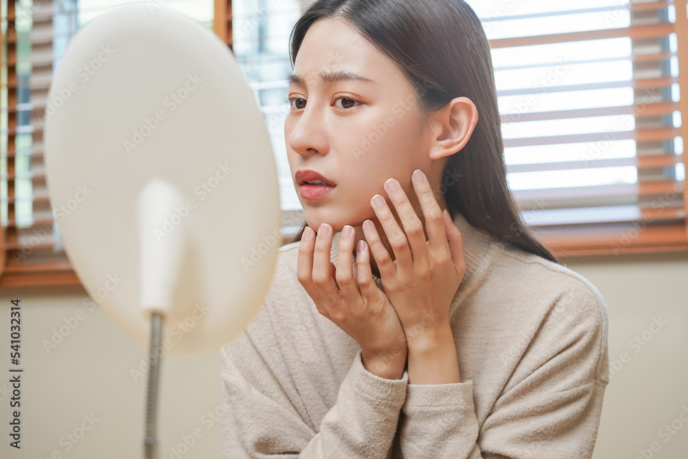 Dermatology, puberty asian young woman, girl looking into mirror, allergy presenting an allergic reaction from cosmetic, red spot or rash on face. Beauty care from skin problem by medical treatment. Dermatology, puberty asian young woman, girl looking into mirror, allergy presenting an allergic reaction from cosmetic, red spot or rash on face. Beauty care from skin problem by medical treatment.