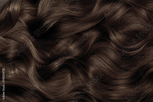 Brown hair close-up as a background. Women's long brown hair. Beautifully styled wavy shiny curls. Hair coloring. Hairdressing procedures, extension. photo