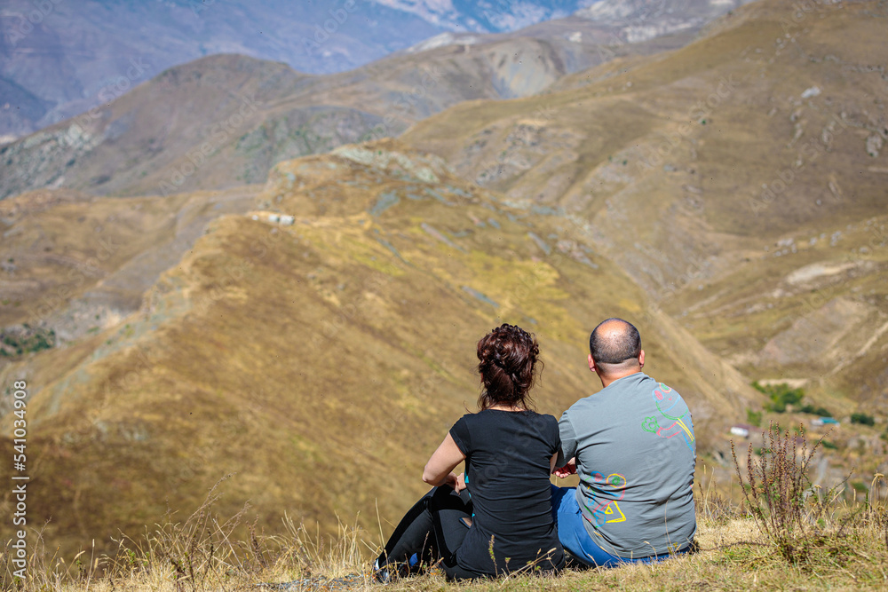 A man and a girl are sitting on a hill in the mountains. A loving couple enjoys the scenery. Caucasus mountains, Ossetia. A man and a girl are sitting on a hill in the mountains. A loving couple enjoys the scenery. Caucasus mountains, Ossetia.