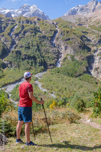A hiker with canes looks into the distance on a path in the mountains to the waterfalls.