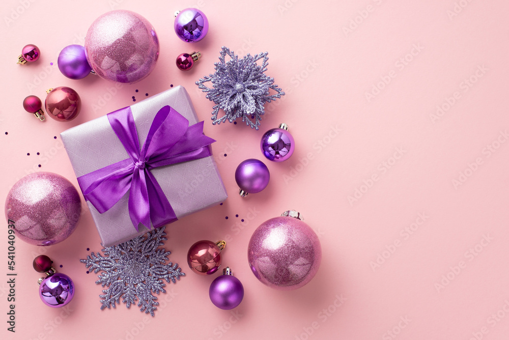 New Year concept. Top view photo of big purple present box with ribbon bow pink violet baubles snowflake flower ornaments and confetti on isolated pastel pink background New Year concept. Top view photo of big purple present box with ribbon bow pink violet baubles snowflake flower ornaments and confetti on isolated pastel pink background