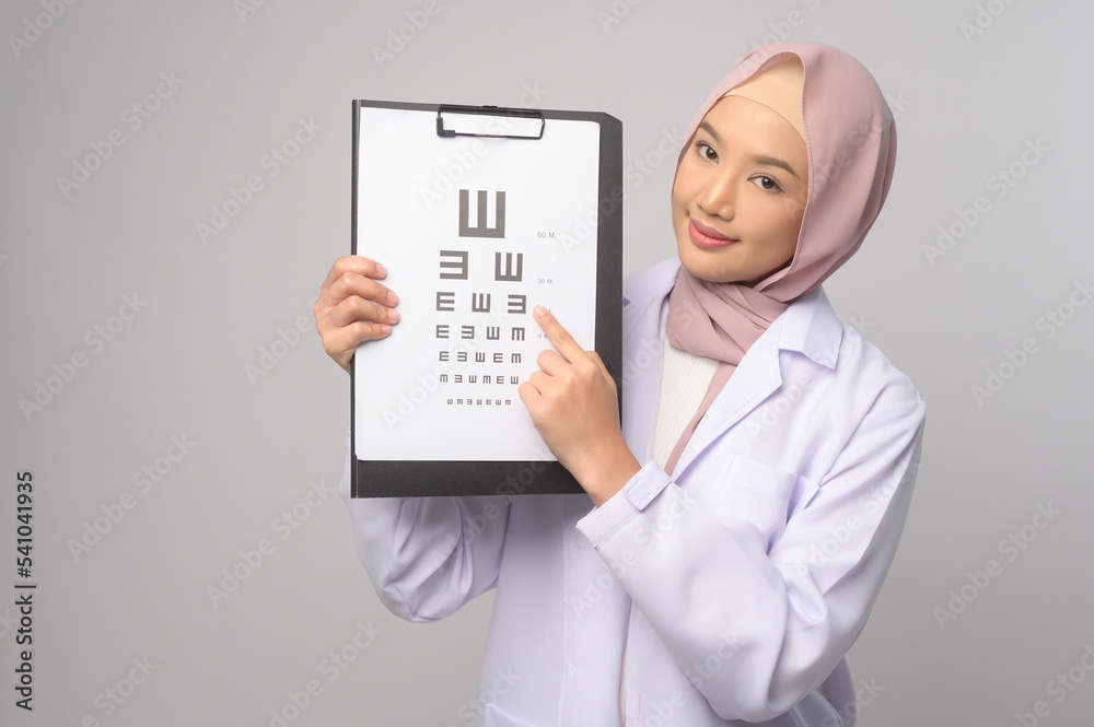 Young muslim female ophthalmologist with glasses holding eye chart over blue background studio, healthcare concept. Young muslim female ophthalmologist with glasses holding eye chart over blue background studio, healthcare concept.