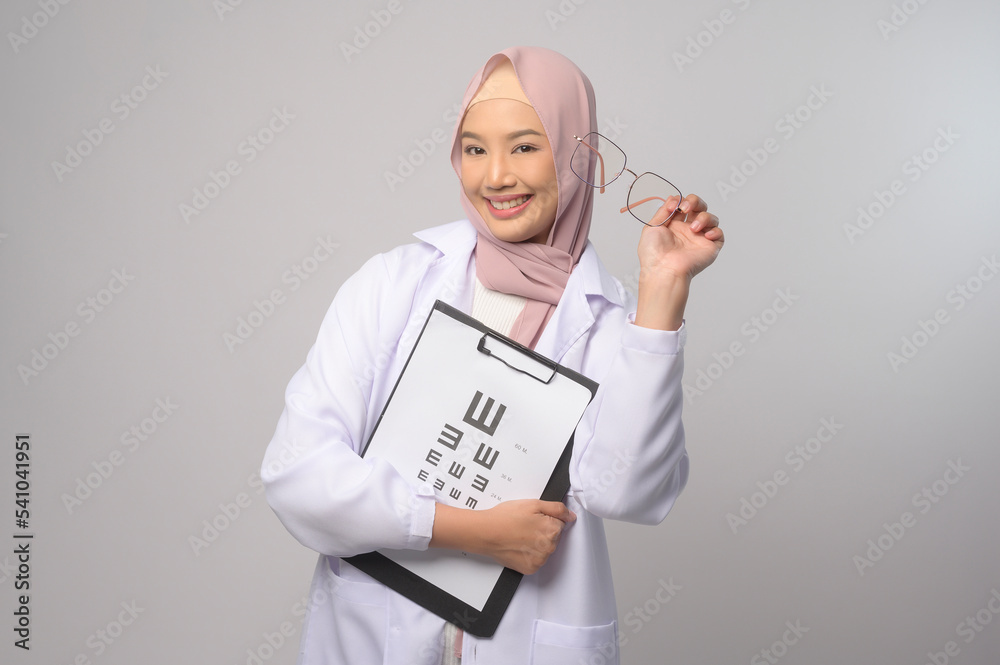 Young muslim female ophthalmologist with glasses holding eye chart over blue background studio, healthcare concept. Young muslim female ophthalmologist with glasses holding eye chart over blue background studio, healthcare concept.