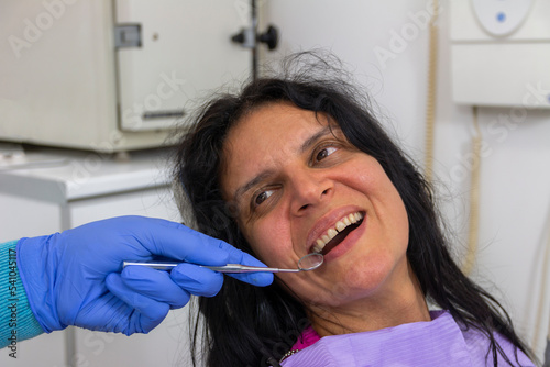A middle-aged woman sitting in medical chair while dentist fixing her teeth at dental clinic