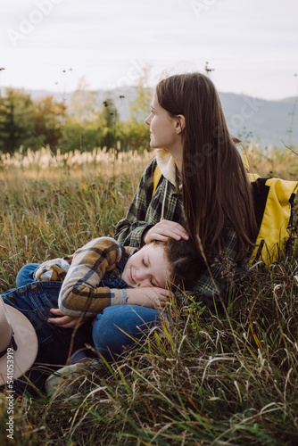 Loving young mother and pretty little daughter child sitting in grass on background beautiful mountains autumn. Adorable small girl kid with smiling mommy enjoy calm nature. Family weekend concept
