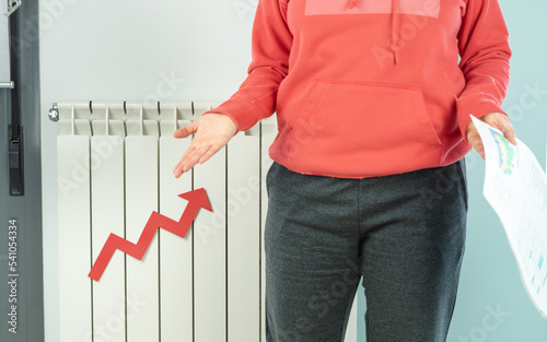 Woman with bill in front of heating radiator asks for explanation for price increase. Copy space.