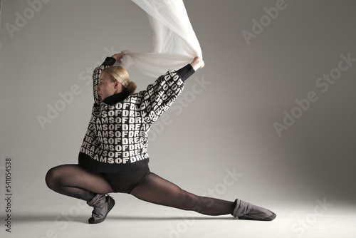 Fototapeta Naklejka Na Ścianę i Meble -  Ballerina Dancing with Silk Fabric, Modern Ballet Dancer with Waving white fabric, Gray Background. With text on sweater DREAMS OF