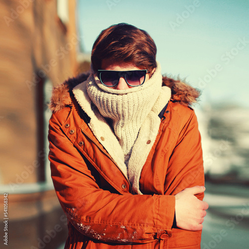 Winter portrait of man freezes hides his head and warms body in the city