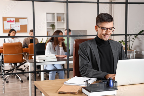 Smiling businessman working with laptop at table in office