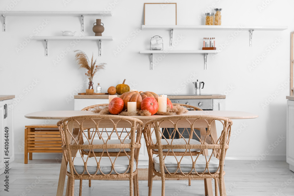 Dining table with pumpkins, pampas grass and burning candles in light kitchen