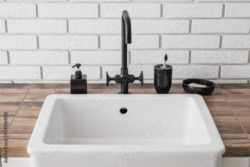 Bath accessories and sink on table near white brick wall